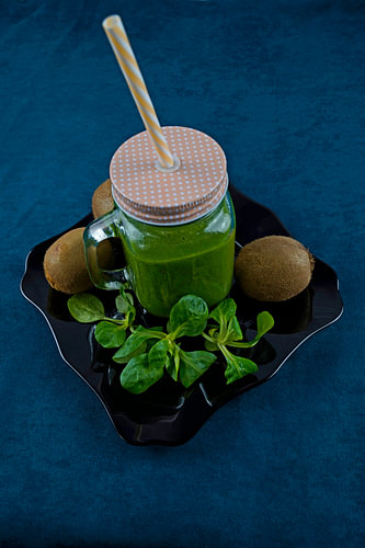 Leaf salad and kiwi smoothie on black plate decorated with kiwi and field salad