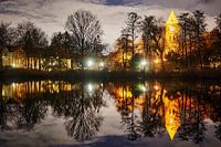 Une église de village historique éclairée par des lampes la nuit et se reflétant dans un étang.