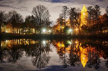 Une église de village historique éclairée par des lampes la nuit et se reflétant dans un étang. sur Michaela Bechinie