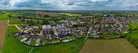 Panoramisch uitzicht op een vredig Limburgs dorp te midden van glooiende heuvels, groene velden en karakteristieke woningen onder een dramatisch wolkendek in de lente. van byphotographyms thumbnail