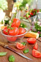 Fresh tomatoes lie in a colander on a wooden tray