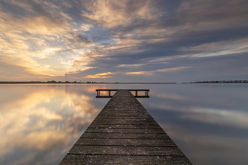 Long jetty in calm lake near Den Oever is surrounded by beautiful clouds