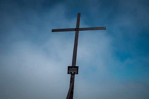 Berggipfelkreuz – Minimalistische Silhouette vor einem dramatischen Wolkenhimmel