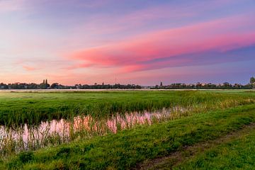 Roze wolken bij zonsondergang boven een weiland. van Rob Baken