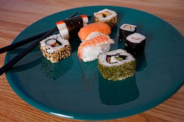 Sushi angeordnet auf einem grünen Teller mit Stäbchen