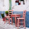 Griechische Stühle in einer pastellfarbenen Straße auf Samos von Angelique van Esch