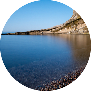 stijle rotswand in de zee met spiegelend water van Eline Oostingh