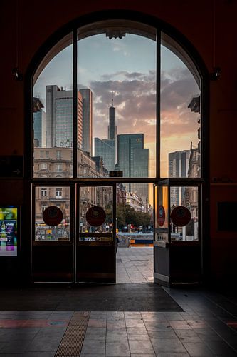 Zicht door de hoofdingang van het Centraal Station van Frankfurt naar de skyline bij zonsopgang