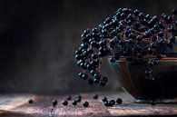 Black elderberries bunch (Sambucus nigra) in an old clay bowl and some berries on a rustic wooden ta by Maren Winter thumbnail
