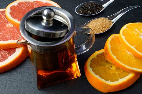 Zwarte thee in een pot, versierd met schijfjes grapefruit en sinaasappel