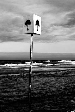 Schwarz-Weiß-Foto eines Schildes mit Regenschirm am Strand von Wim Stolwerk