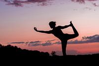 Silhouette van een yoga lerares in pose bij ondergaande zon.