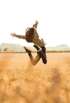 Meisje springt vreugdevol op uit een gouden graan veld van Lex Overtoom
