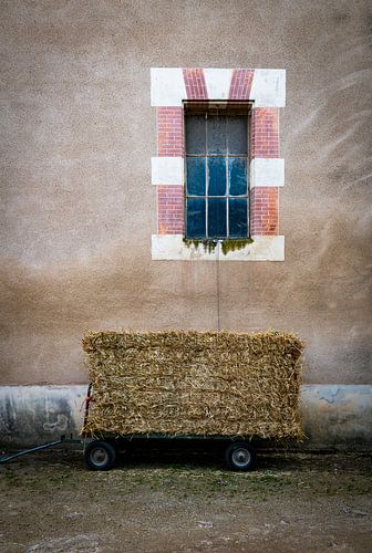 Rustic Farm Scene With Hay Bale Wagon Beside A Beige Wall And Old Window Facade by ChrisWillemsen