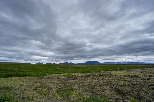 IJsland - Bewolkte lucht boven intens groene, met planten bedekte weiden en besneeuwde bergweiden