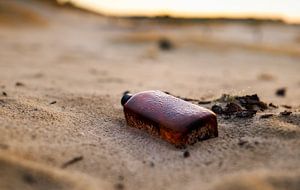 Glazen Fles met Dauwdruppels: Magische Reflecties op een Zandverstuiving bij Zonsopkomst