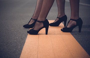 Frauenbeine mit High Heels auf einer Straße von Denny Gruner