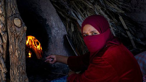Woman baking bread in an open fire oven by Rene Siebring