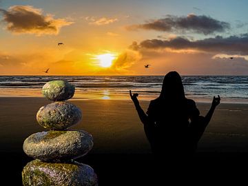 Balancesteine am Strand mit Sonnenuntergang und einer Frau die Meditiert von Animaflora PicsStock