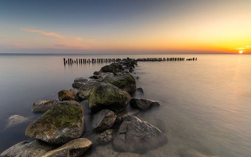 Een waterkering van grote stenen en paaltjes in het IJsselmeer bij zonsopkomst