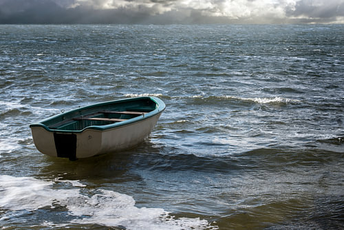 Leeres Ruderboot treibt einsam auf den Meereswellen zu den Wolken am weiten Horizont, Meereslandscha