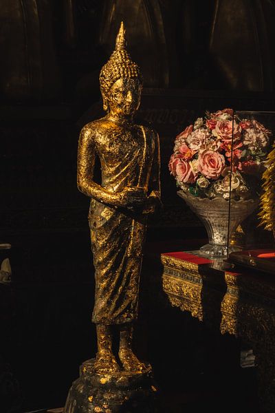 Shiny Buddha statue in front of Thai flowers by NZME Photography