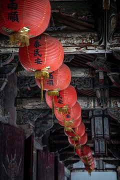 Red lanterns along the ceiling of a temple by Mickéle Godderis