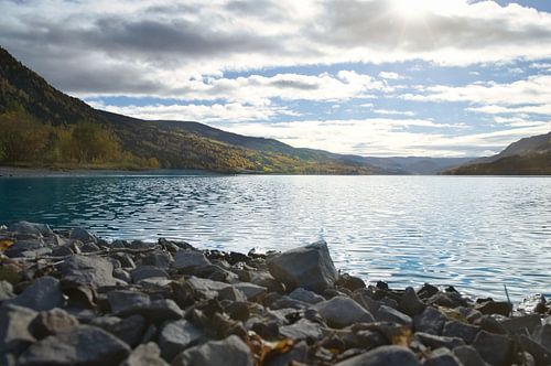 Rustig bergmeer met herfstheuvels en rotsen in het heldere water
