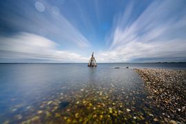 Sculptures on the coast beneath dancing clouds above calm waters by Fotografiecor .nl