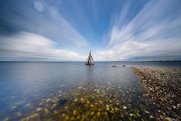 Sculptures on the coast beneath dancing clouds above calm waters
