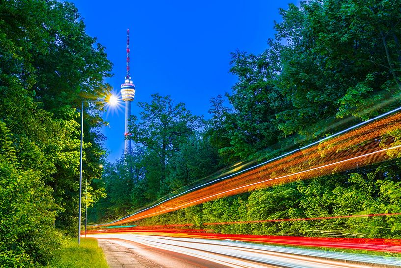 Deutschland, Stuttgarter Fernsehturm bei Nacht neben grünem Wald und beleuchteten Lichtern der Straß von adventure-photos