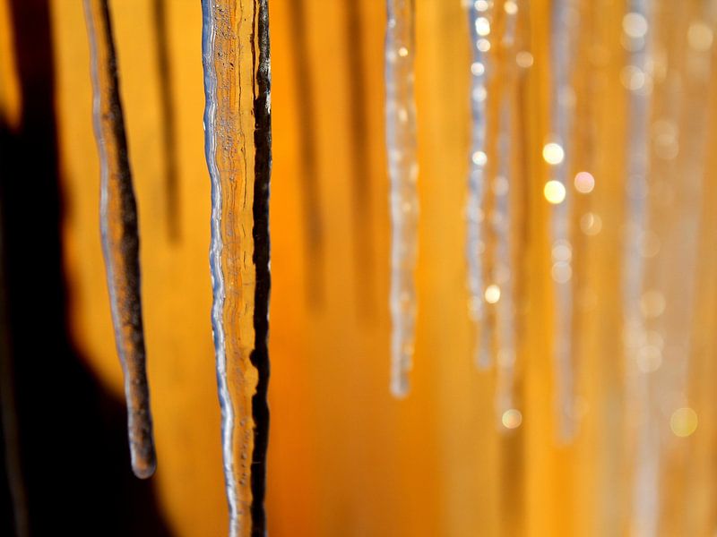 Frozen icicles in front of a yellow wall by Russell