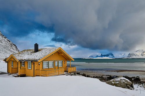 wooden yellow house or hut in winter landscape in stormy weather with sea and mountains