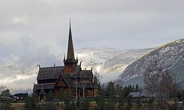 Staafkerk van Lom in Noorwegen met besneeuwde bergen op de achtergrond.