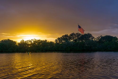 USA, Florida, Fantastische oranje zonsondergang op water, groene planten en Amerikaanse vlag met reflecties