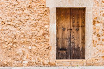 Vue détaillée d'un mur de pierre d'une maison méditerranéenne avec une vieille porte en bois sur Alex Winter