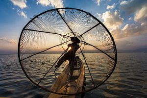 Visser die met traditionele boot op het Inle meer in Myanmar op ouderwetse wijze met een vis korf vi
