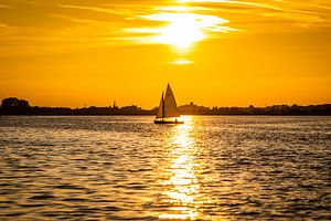 Zeilboot op een meer tegen de rood /oranje lucht van een zonsondergang van Jan Hermsen