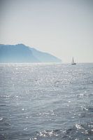 A sailboat sails off the coast of an island in the sea