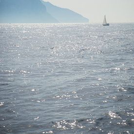 A sailboat sails off the coast of an island in the sea by Esther esbes - kleurrijke reisfotografie