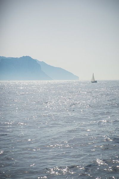A sailboat sails off the coast of an island in the sea by Esther esbes - kleurrijke reisfotografie