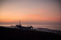Indonesian fisherman pushing his boat ashore in Kubu, Bali, Indonesia, during sunset.
