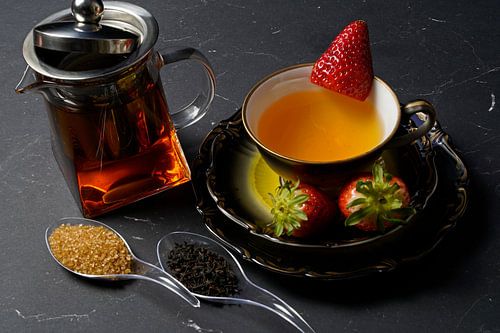 Zwarte thee met aardbei in een kopje en een glazen pot met thee