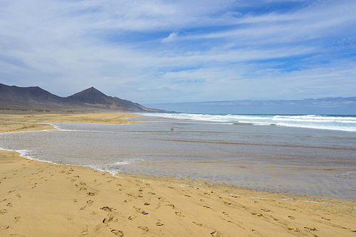Des vagues qui s'étendent loin sur la plage, le long du littoral peu profond de Playa de Cofete