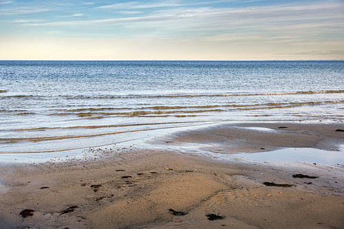 Nasser Sandstrand, ruhige Wellen und Blick über das Wasser zum Horizont an der Ostsee in Norddeutsch