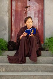 Chinesische Nonne auf den Stufen vor einer burgunderroten Tür in Pingyao in China von Cindy Mulder