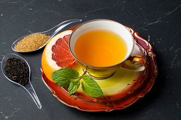 Schwarzer Tee mit Grapefruit in einer Tasse und Löffel mit Rohrzucker