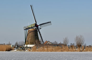 Oer Hollands winterlandschap met een klassieke windmolen met rieten kap langs het water van de Wijde