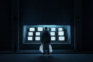 Un jeune homme, sacs blancs à la main, se tient devant une vitrine de télévision dans la nuit