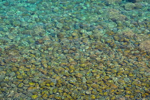 Une eau de mer cristalline en Sicile, parsemée de galets multicolores